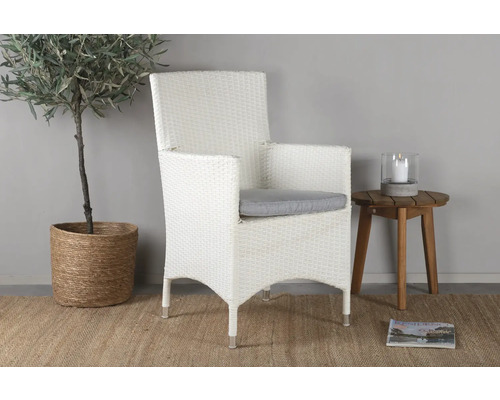 Flätad trädgårdsfåtölj med sittdyna bredvid sidobord, krukväxt och tidning