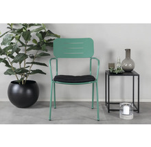 Scen med en grön metallstol med armstöd, en svart sittdyna, en krukväxt i en svart kruka och ett sidobord med dekoration.