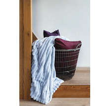 Dekorativt arrangemang med en mjuk filt, prydnadskuddar och en metallkorg på en trätrappa.