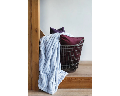 Dekorativt arrangemang med en mjuk filt, prydnadskuddar och en metallkorg på en trätrappa.