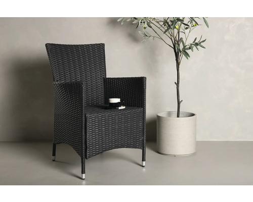 Flätad stol med armstöd och dryckeshållare bredvid en krukväxt.