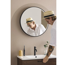 Ett badrum med en rund spegel, ett handfat, en kran och en person.