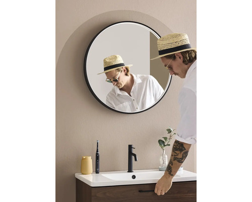 Ett badrum med en rund spegel, ett handfat, en kran och en person.