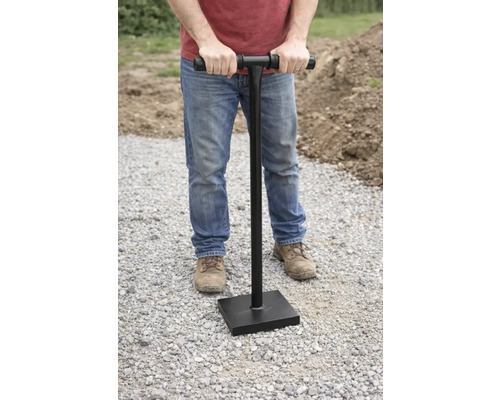 En man använder en handstamp för att packa jorden.