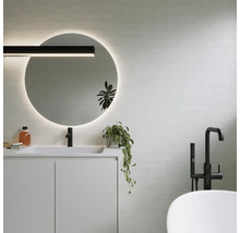 Modernt badrum med rund spegel, tvättställ, armatur och badkar.