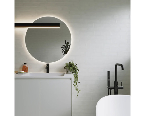 Modernt badrum med rund spegel, tvättställ, armatur och badkar.