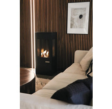 Modern svart braskamin framför en vägg av träribbor med integrerade ljuslister i ett hemtrevligt vardagsrum med soffa.