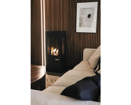 Modern svart braskamin framför en vägg av träribbor med integrerade ljuslister i ett hemtrevligt vardagsrum med soffa.