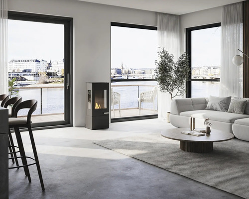 Modern svart braskamin i ett ljust, rymligt vardagsrum med stora fönsterpartier, ljus soffa och utsikt över vatten.