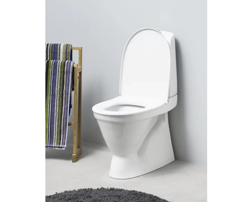 Vit golvstående toalett med öppet lock bredvid en handdukshållare med handdukar