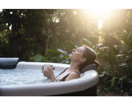 Kvinna kopplar av i en bubbelpool med en kopp i handen mitt i naturen.