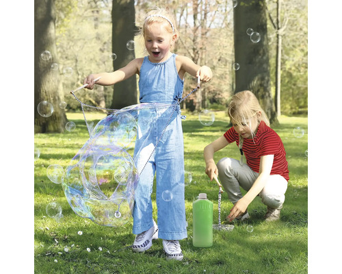 Två barn leker i parken med ett såpbubbelset och skapar stora såpbubblor.