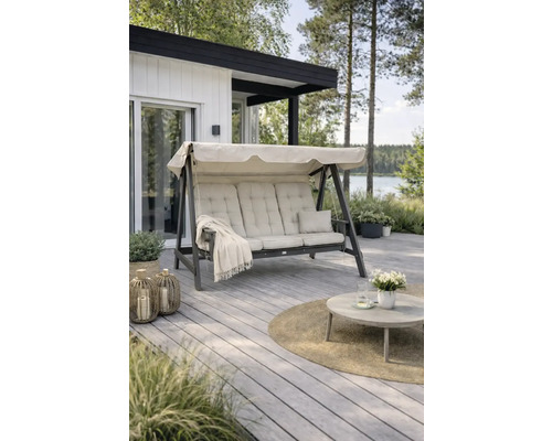 Hammock EDENWOOD 3-sits utan tak & dynor antracit Tre-sits trädgårdsgunga med beige dynor och soltak på en träterrass. Modern uteplats med bord, lyktor och utsikt över en sjö.