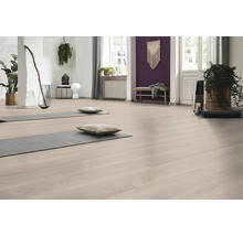 Ljust rum med golv i trälook, två grå yogamattor med kuddar, krukväxter och en lila fondvägg.