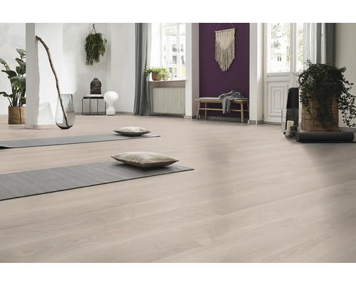 Ljust rum med golv i trälook, två grå yogamattor med kuddar, krukväxter och en lila fondvägg.