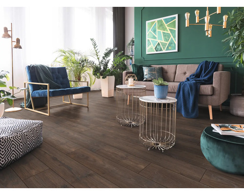 Vardagsrum med mörkt golv i trälook, grå soffa, blå fåtölj och grön vägg med inomhusväxter. Modern och ljus inredning.