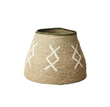 Flätat krukskydd av naturfiber med vitt geometriskt mönster och grön kant.