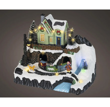 Julminiatyrlandskap med belyst hus, tåg, barn, hund och snötäckt bergsmiljö.