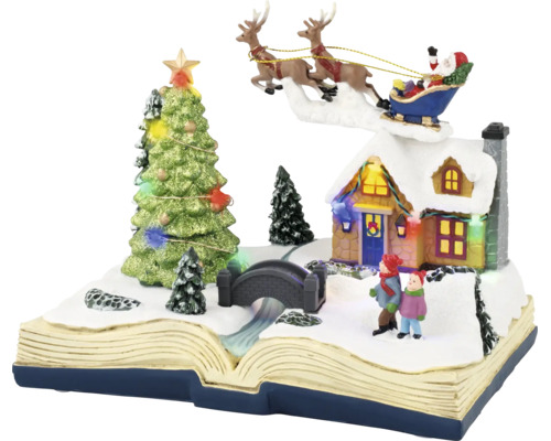 Juldekoration i form av en öppen bok med snöigt vinterlandskap, upplyst hus, julgran och jultomte i släde.