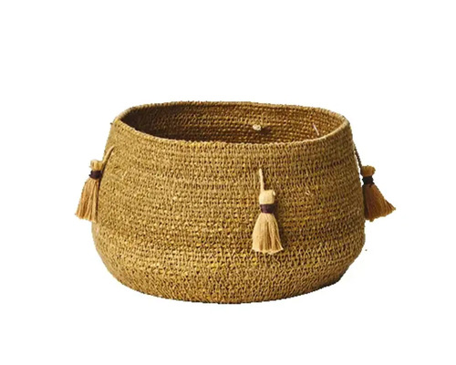 Ockrafärgad flätad förvaringskorg av jute med dekorativa tofsar.
