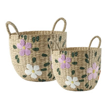 Set med två flätade korgar av sjögräs med broderade lila och vita blommor och gröna blad, var och en med två handtag.