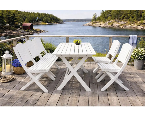 Trädgårdsmöbler i vitt trä på en altan vid vatten, bestående av ett bord med kryssben, en bänk och två fällstolar.