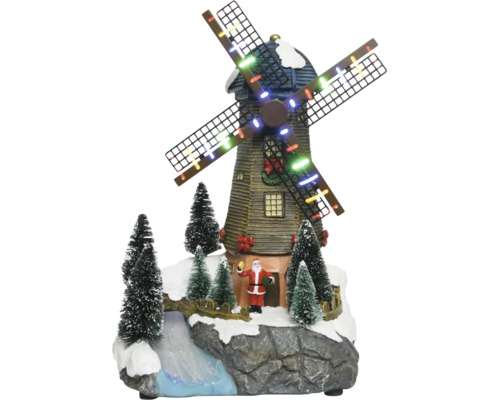 Juldekoration med en belyst väderkvarn, tomtefigur, snöklädda granar och en bäck på en klippbas.