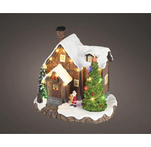 Miniatyrjulhus i trä med snötäckt tak, belyst julgran och liten jultomtefigur.