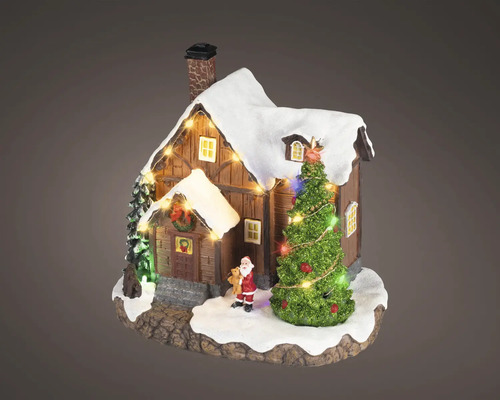 Miniatyrjulhus i trä med snötäckt tak, belyst julgran och liten jultomtefigur.