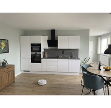 Modernt kök med vita skåp, grått stänkskydd, runt träbord, blå stolar och robotdammsugare på ljust trägolv.