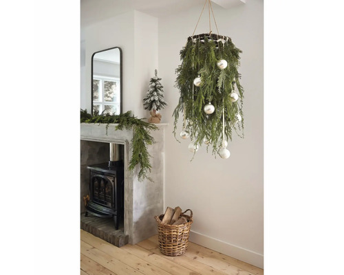 Ljust vardagsrum med hängande juldekoration av grankvistar, en kamin och en flätad korg med vedträn.