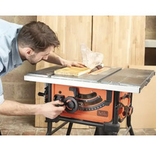 Man som använder en Black och Decker bordscirkelsåg för att kapa en träskiva i en ljus verkstad.
