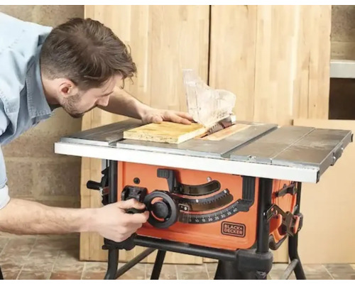 Man som använder en Black och Decker bordscirkelsåg för att kapa en träskiva i en ljus verkstad.