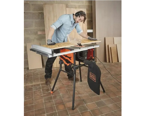 Man med hörselskydd och handskar använder en Black and Decker bordscirkelsåg med stativ för att kapa en träskiva.