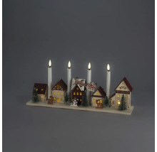 Juldekoration i trä med en miniatyrby, upplysta hus, granar, renar och fyra vita elektriska ljus på en träsockel.