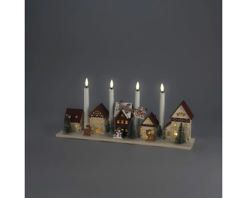 Juldekoration i trä med en miniatyrby, upplysta hus, granar, renar och fyra vita elektriska ljus på en träsockel.