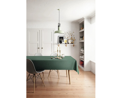 Ljust matrum med grön duk på ett träbord, modern stol, hängande taklampa och juldekorationer på en vägghylla.