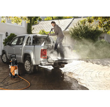 En man rengör flaket på en pickup med en Stihl högtryckstvätt på en stenlagd uppfart.