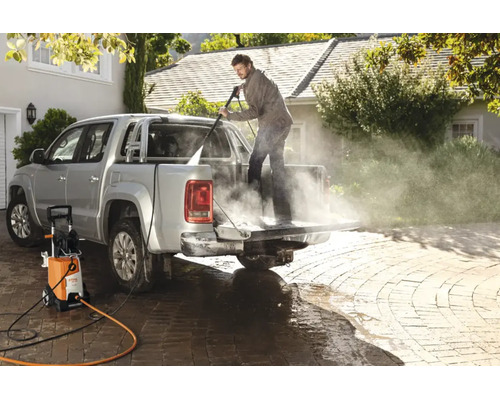 En man rengör flaket på en pickup med en Stihl högtryckstvätt på en stenlagd uppfart.