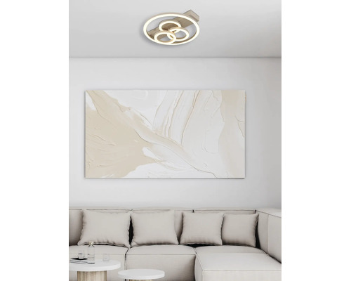 Modern LED-taklampa med fyra ringar i ett ljust vardagsrum ovanför en abstrakt tavla och en soffa.
