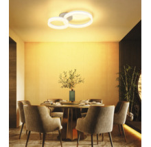 Modern LED-taklampa med två ringar över ett runt matbord i en varmt upplyst, stilren matsal.