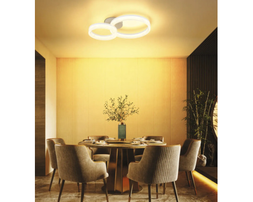 Modern LED-taklampa med två ringar över ett runt matbord i en varmt upplyst, stilren matsal.