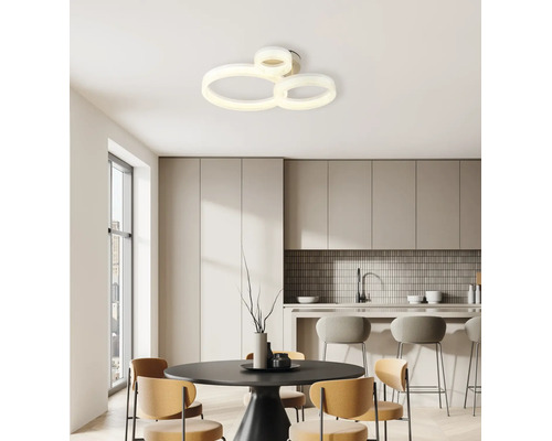 Modern LED-taklampa med tre sammankopplade ringar i ett ljust, minimalistiskt kök med matbord och barstolar.