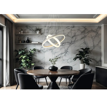 Modern LED-pendellampa med tre sammanflätade ringar över ett runt matbord i trä i ett ljust rum med väggar i marmorlook.