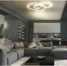 Modern LED-taklampa med fyra ringar i ett rymligt vardagsrum med grå hörnsoffa och modernt kök.