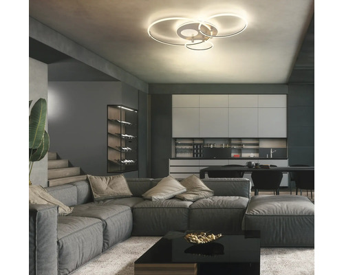 Modern LED-taklampa med fyra ringar i ett rymligt vardagsrum med grå hörnsoffa och modernt kök.