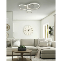 Modern LED-taklampa med tre ringar i ett ljust, organiserat vardagsrum med en soffa och en stor väggklocka.