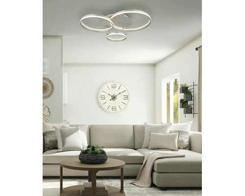 Modern LED-taklampa med tre ringar i ett ljust, organiserat vardagsrum med en soffa och en stor väggklocka.