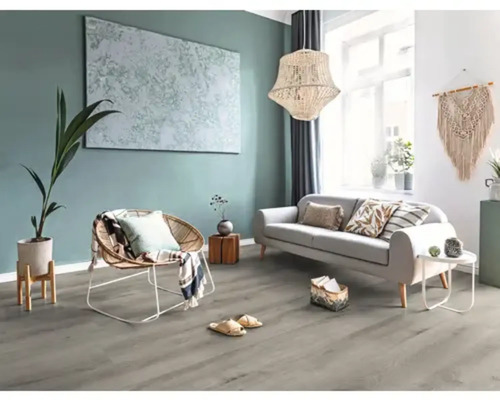 Modernt, ljust vardagsrum med grått laminatgolv i trädekor, ljus soffa, rottingfåtölj och en stor taklampa.