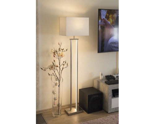 Modern golvlampa med vit textilskärm och integrerad LED-list i ett vardagsrum bredvid en glasvas med grenar.
